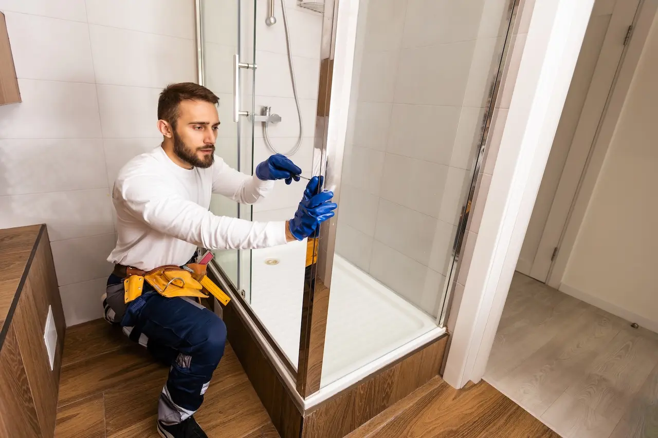 Worker is connecting the glass walls of the shower enclosure with a metal bar.