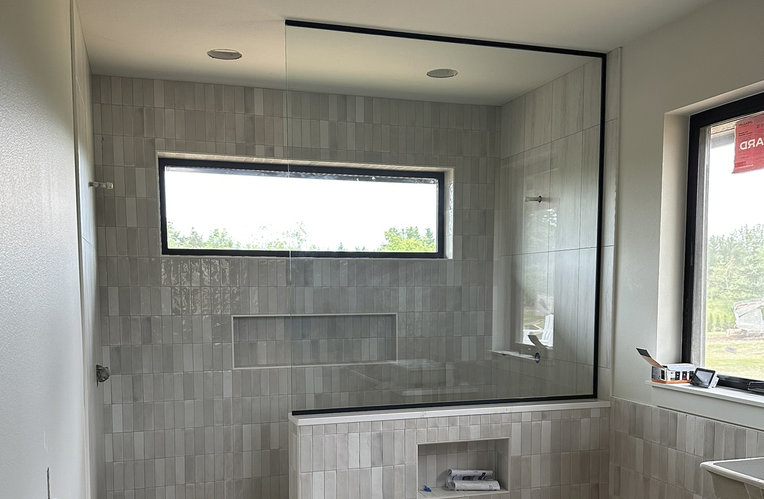 Newly installed frameless glass shower enclosure with matte black hardware and large clear glass panels in a modern tiled bathroom.