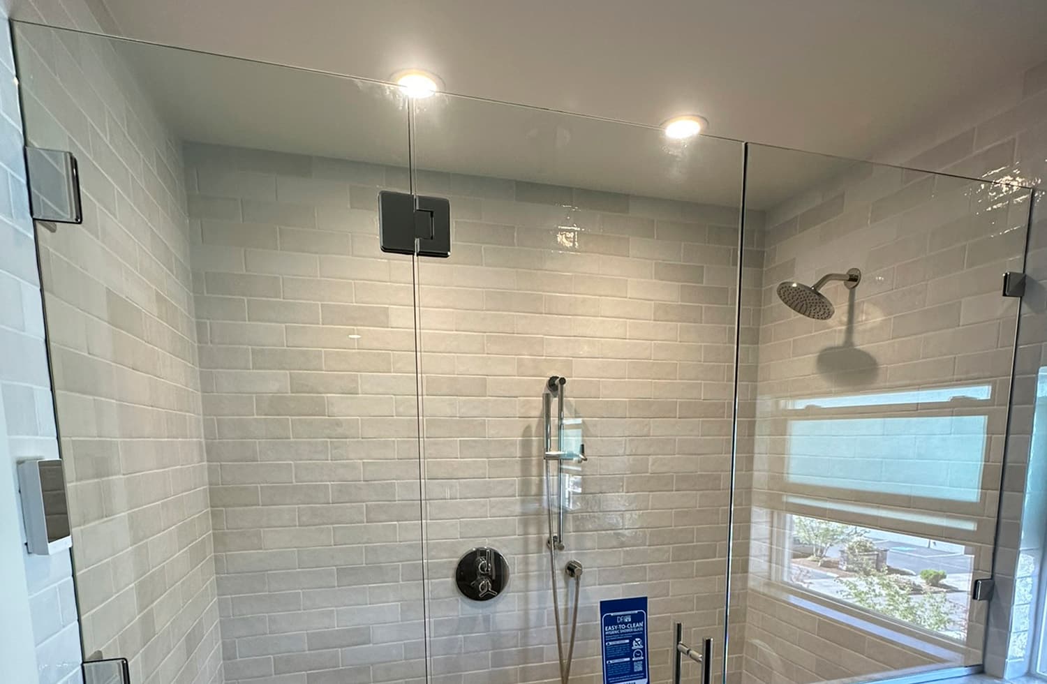 Custom frameless glass shower enclosure with angled panels and brushed metal hardware installed in a modern bathroom with blue subway tile walls.