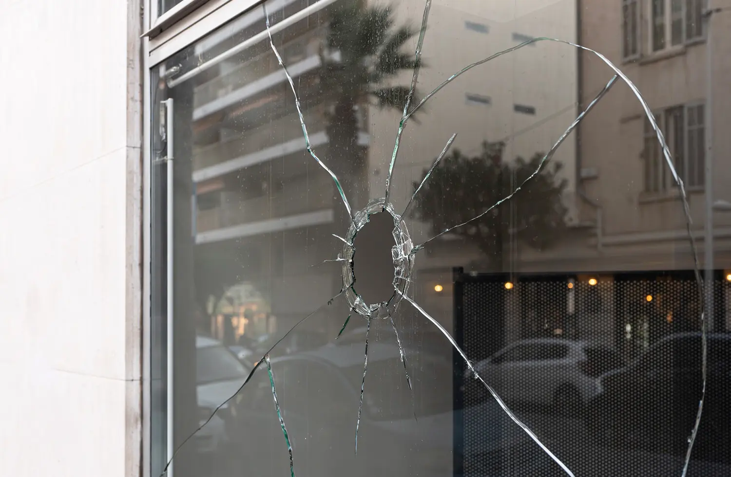 Damaged commercial storefront glass with a large impact hole and spreading cracks, indicating the need for emergency glass repair.